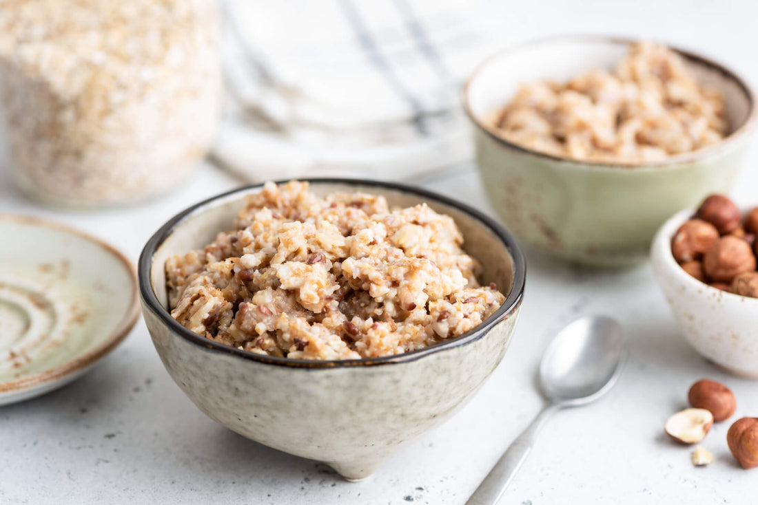 Su un tavolo c'è una ciotola di ceramica piena di porridge, accanto a un cucchiaio, un'altra ciotola di porridge, un piatto e una piccola ciotola di nocciole.