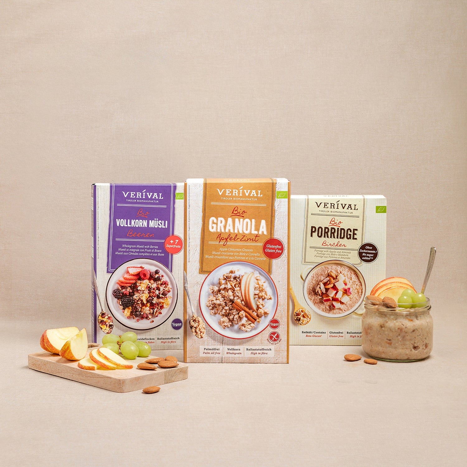 Tre scatole di prodotti per la colazione Verival: muesli integrale, granola e porridge, presentati con frutta fresca e noci su uno sfondo beige.
