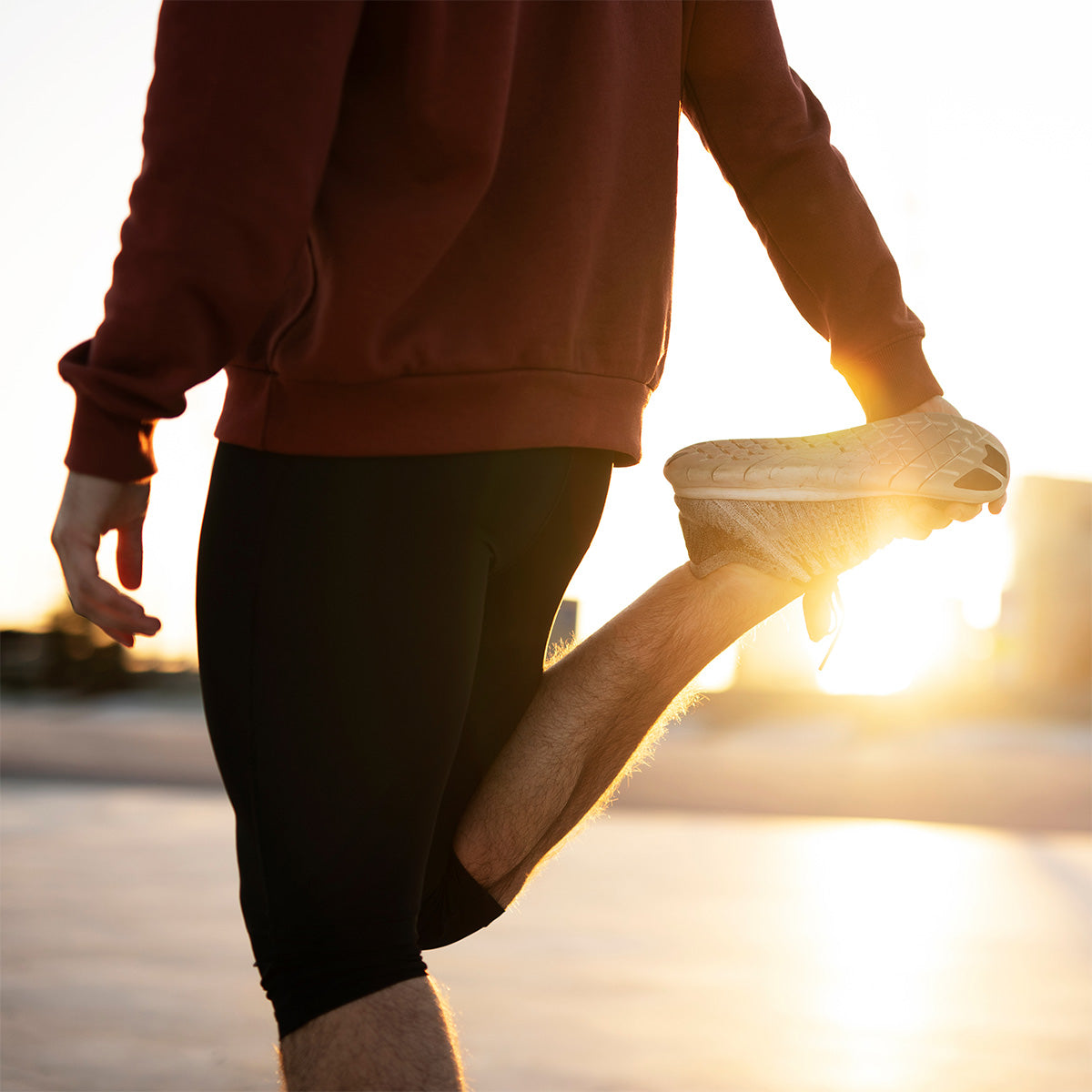 Person, die bei Sonnenaufgang oder Sonnenuntergang im Freien ihr Bein ausstreckt, indem sie den Fuß hinter sich hält, in einem roten Sweatshirt und schwarzen Shorts.
