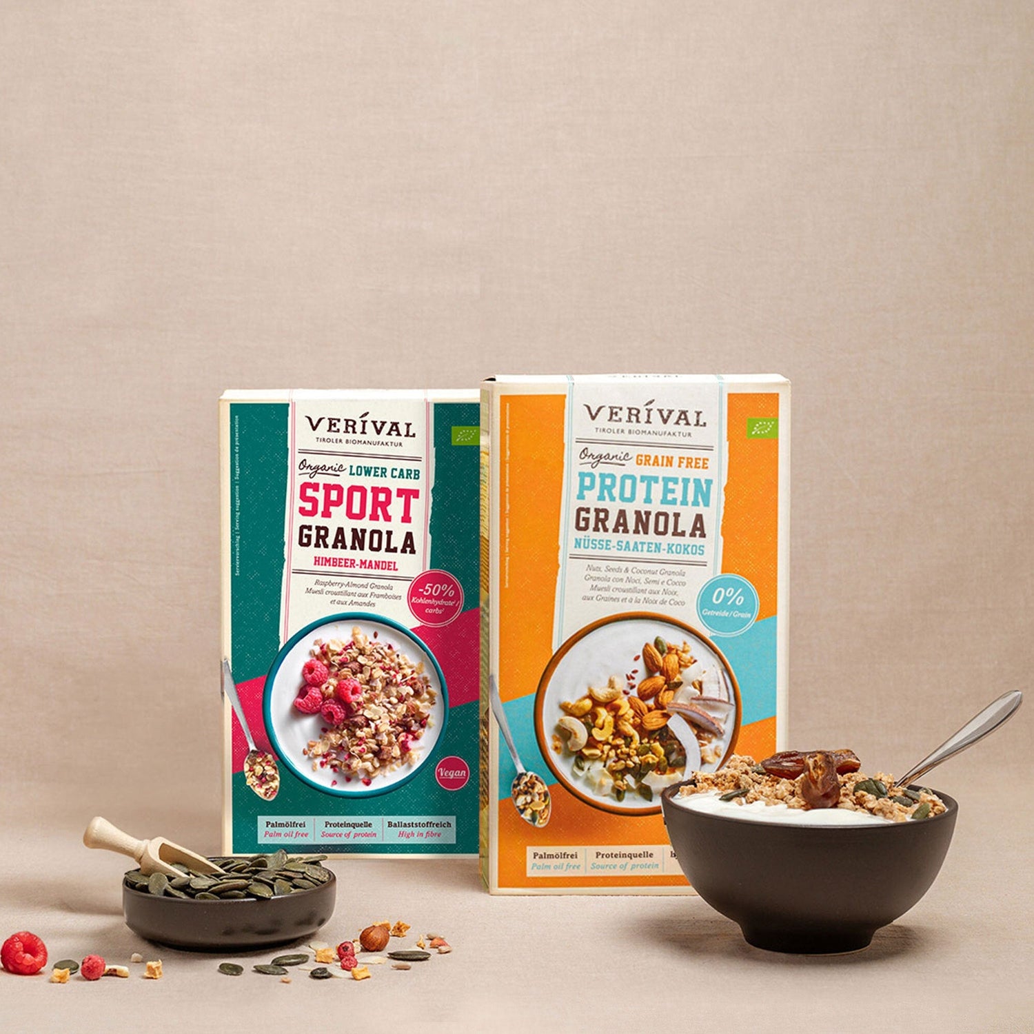 Due scatole di granola Veríval, una granola sportiva e una granola proteica, presentate con una ciotola di granola, semi e bacche su uno sfondo beige.