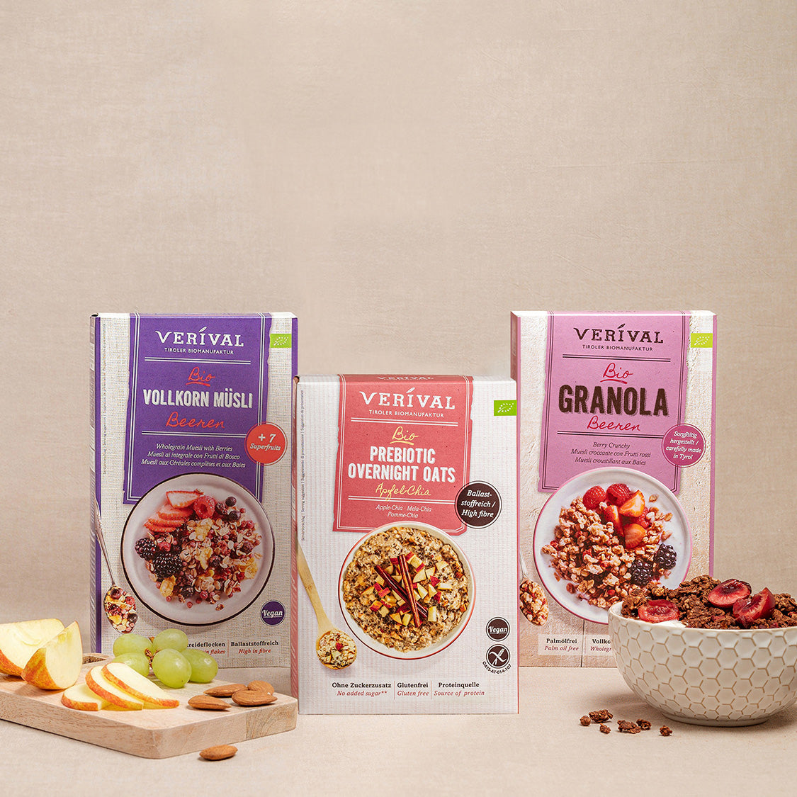 Sono esposte tre scatole di cereali Verival, tra cui muesli integrale, fiocchi d'avena prebiotici per la notte e Schokomax. Davanti a loro, una ciotola di muesli e frutta a fette su un tagliere.