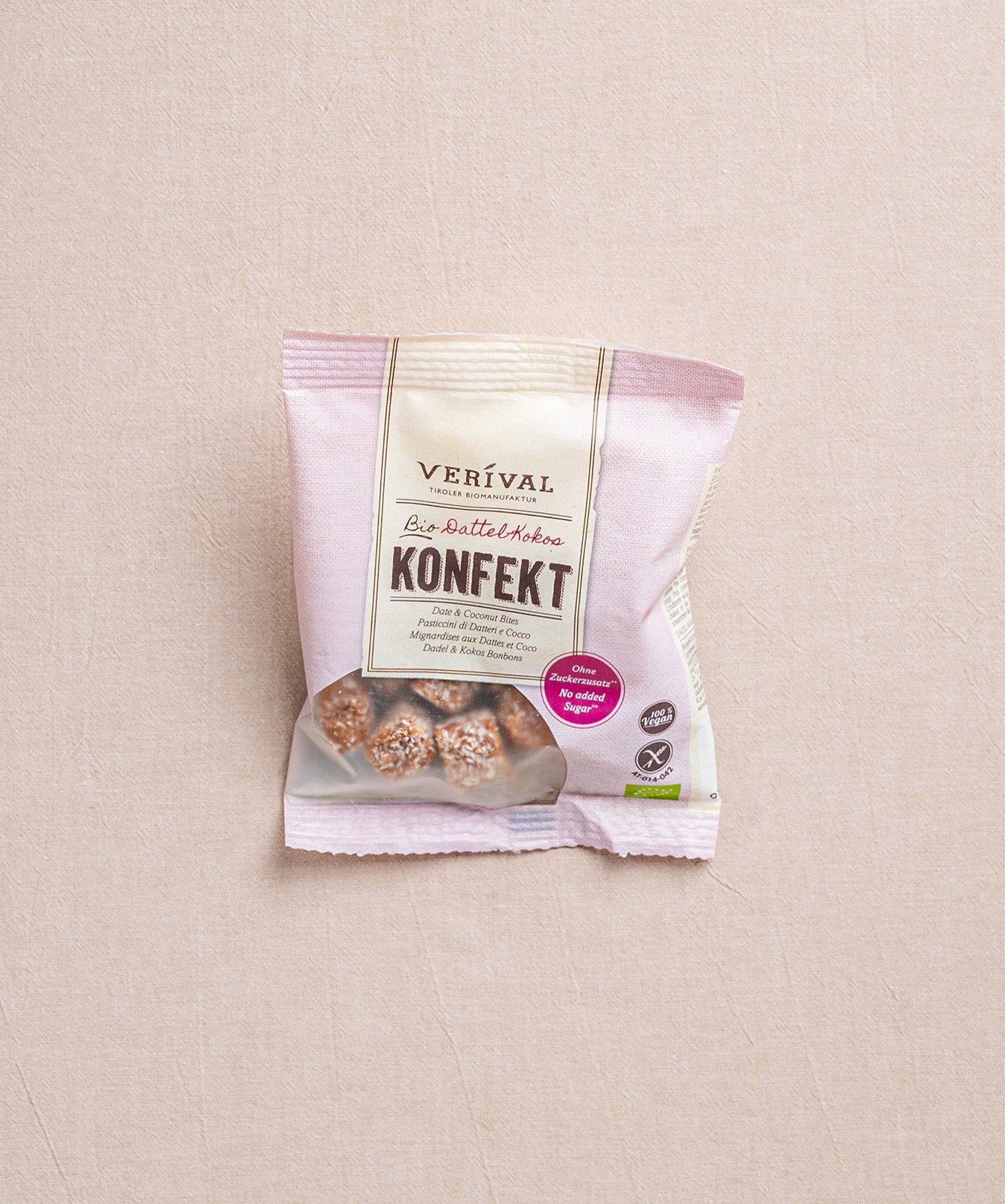Eine Packung Dattel-Kokos Konfekt von Verival Bio liegt auf einem beigen Untergrund. Das Produkt ist eine gesunde Alternative bei Heißhunger auf Süßes.