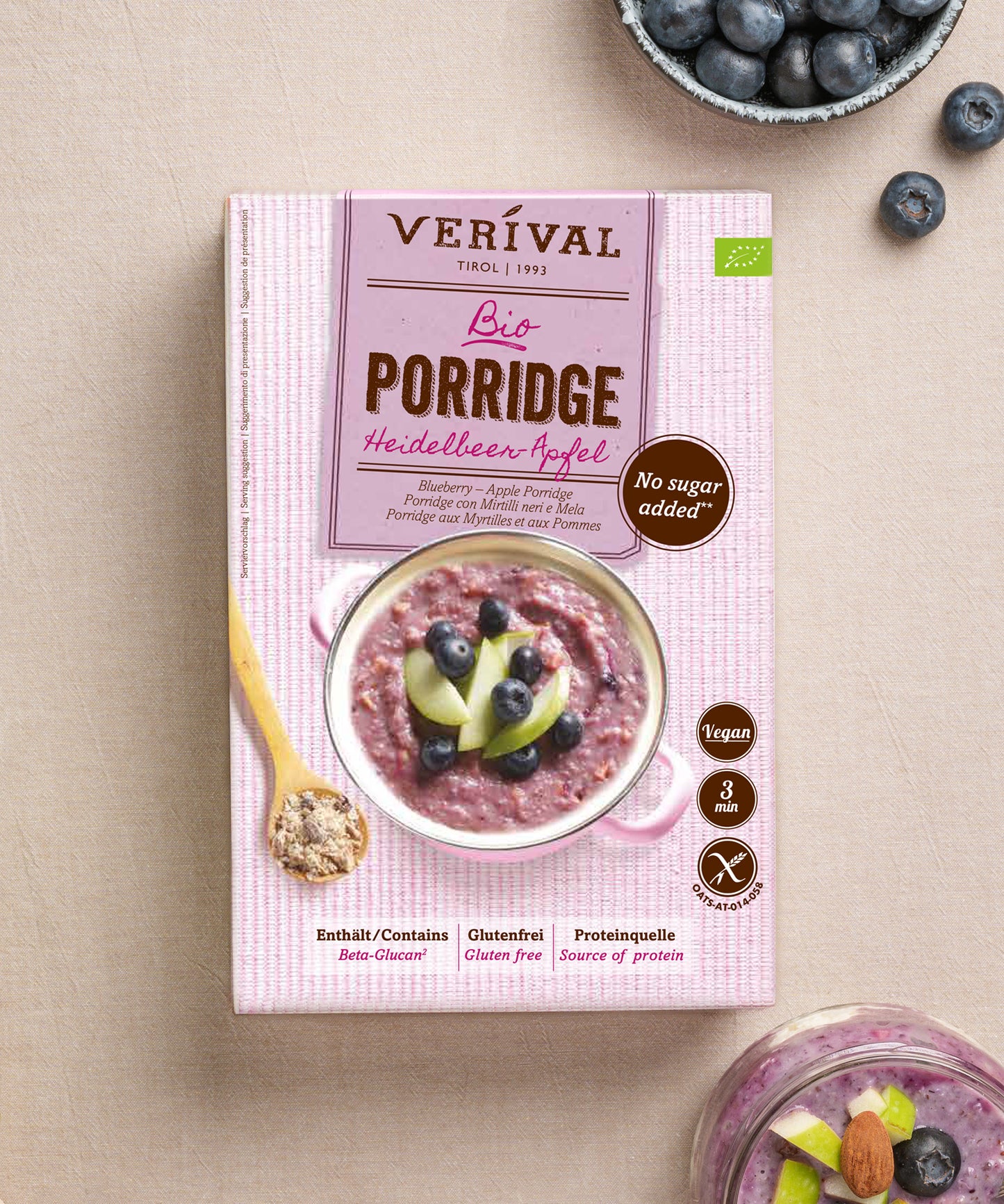 Auf einer hellen Fläche steht eine Dose Bio Heidelbeer-Apfel Porridge der Verival Bio GmbH, begleitet von Heidelbeeren und einem Löffel des ballaststoffreichen, veganen Porridge.