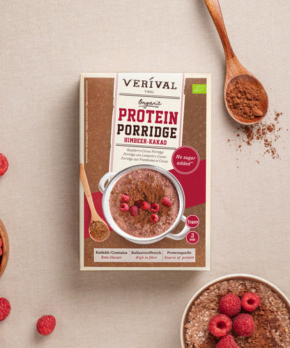 Schachtel Protein Porridge Himbeer-Kakao der Verival Bio GmbH, ein veganes Power-Frühstück mit Himbeeren, Kakaopulver und einem Holzlöffel auf Beige – perfekt als Sport Porridge, um Energie für den Tag zu tanken.