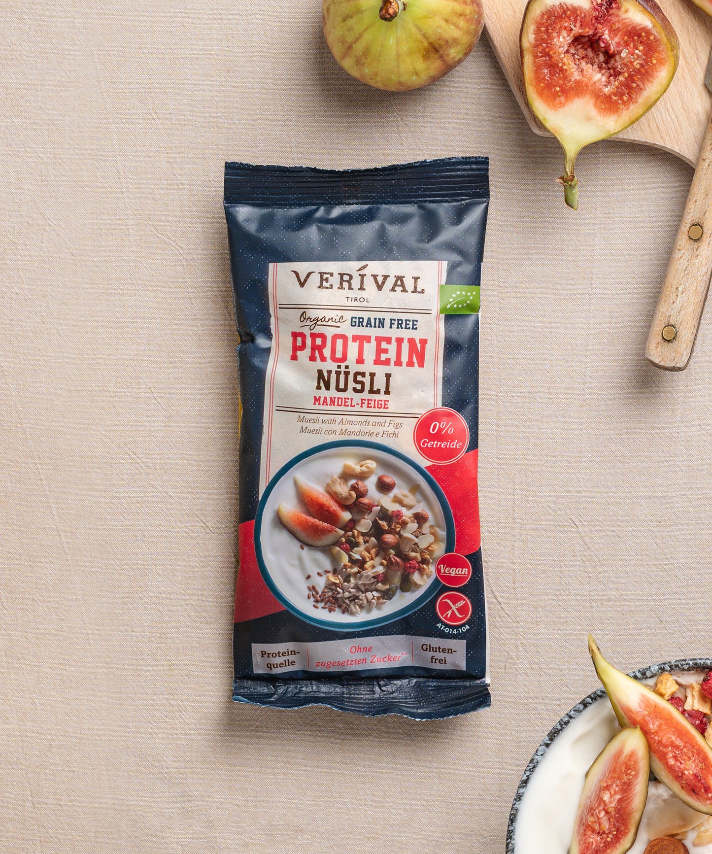 Eine Packung Erdbeer-Chia Porridge der Verival Bio GmbH liegt auf einer beigen Fläche, umgeben von frischen Erdbeeren und einer Schüssel Porridge und ist somit ideal für ein vollwertiges Frühstück.