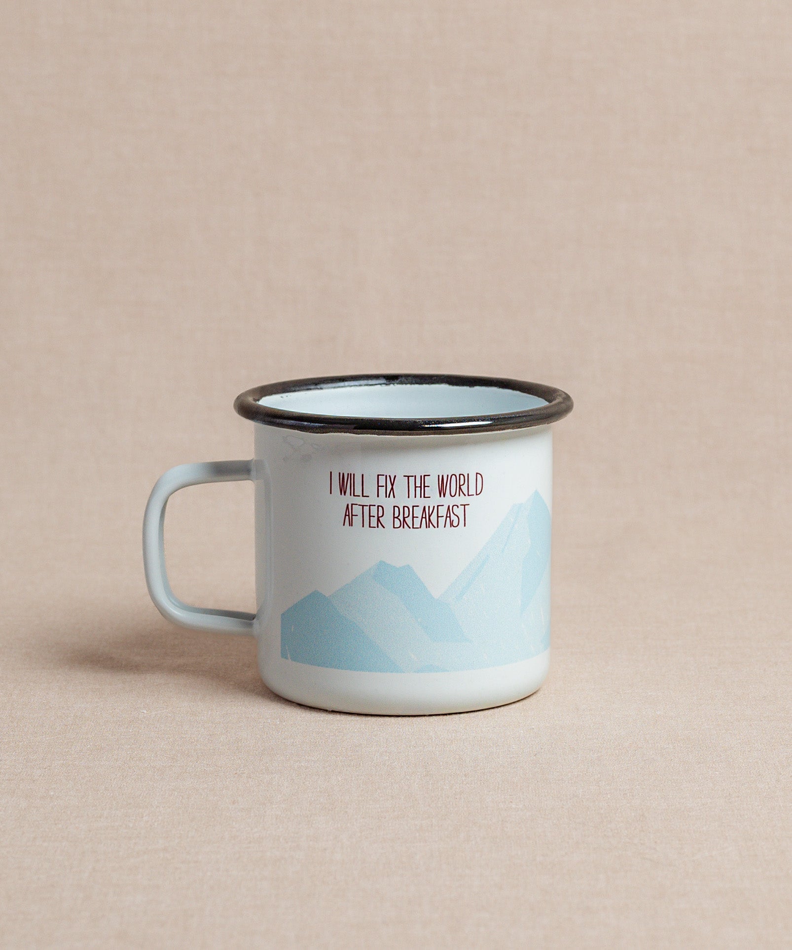 Die Emaille-Tasse von Verival Bio ist hellblaumit schwarzem Rand und Berggrafik. Sie trägt das Zitat „I will fix the world after breakfast“ in Rot und Schwarz – perfekt, um den Morgenkaffee zu genießen und dabei von Bergabenteuern zu träumen.