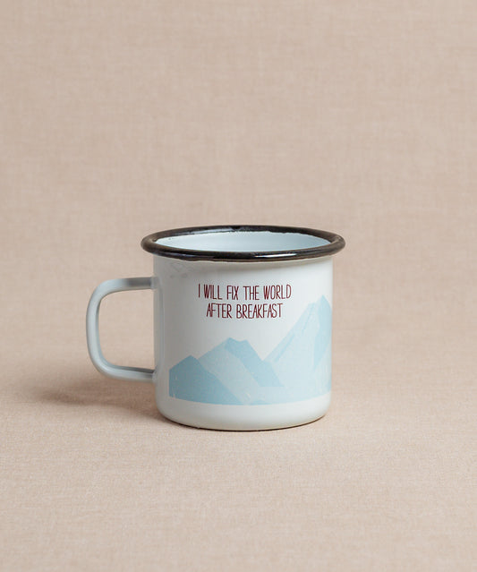Die Emaille-Tasse von Verival Bio ist hellblaumit schwarzem Rand und Berggrafik. Sie trägt das Zitat „I will fix the world after breakfast“ in Rot und Schwarz – perfekt, um den Morgenkaffee zu genießen und dabei von Bergabenteuern zu träumen.