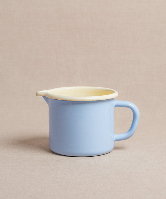 Ein Schnabeltopf von Riess in Hellblau mit Ausguss und Henkel steht auf einer beigen Flächeund ist bereit zum Erwärmen von Milch.