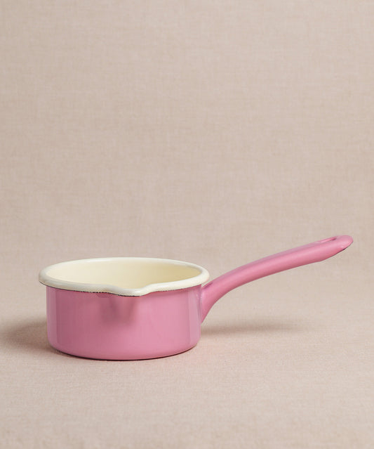 Ein kleiner rosa Emaille-Milchtopf von Riess mit langem Stiel und cremefarbener Innenseite steht auf einer neutralen Oberfläche. Der Topf ist ideal zum Erwärmen von Milch oder zur Zubereitung von Porridge.