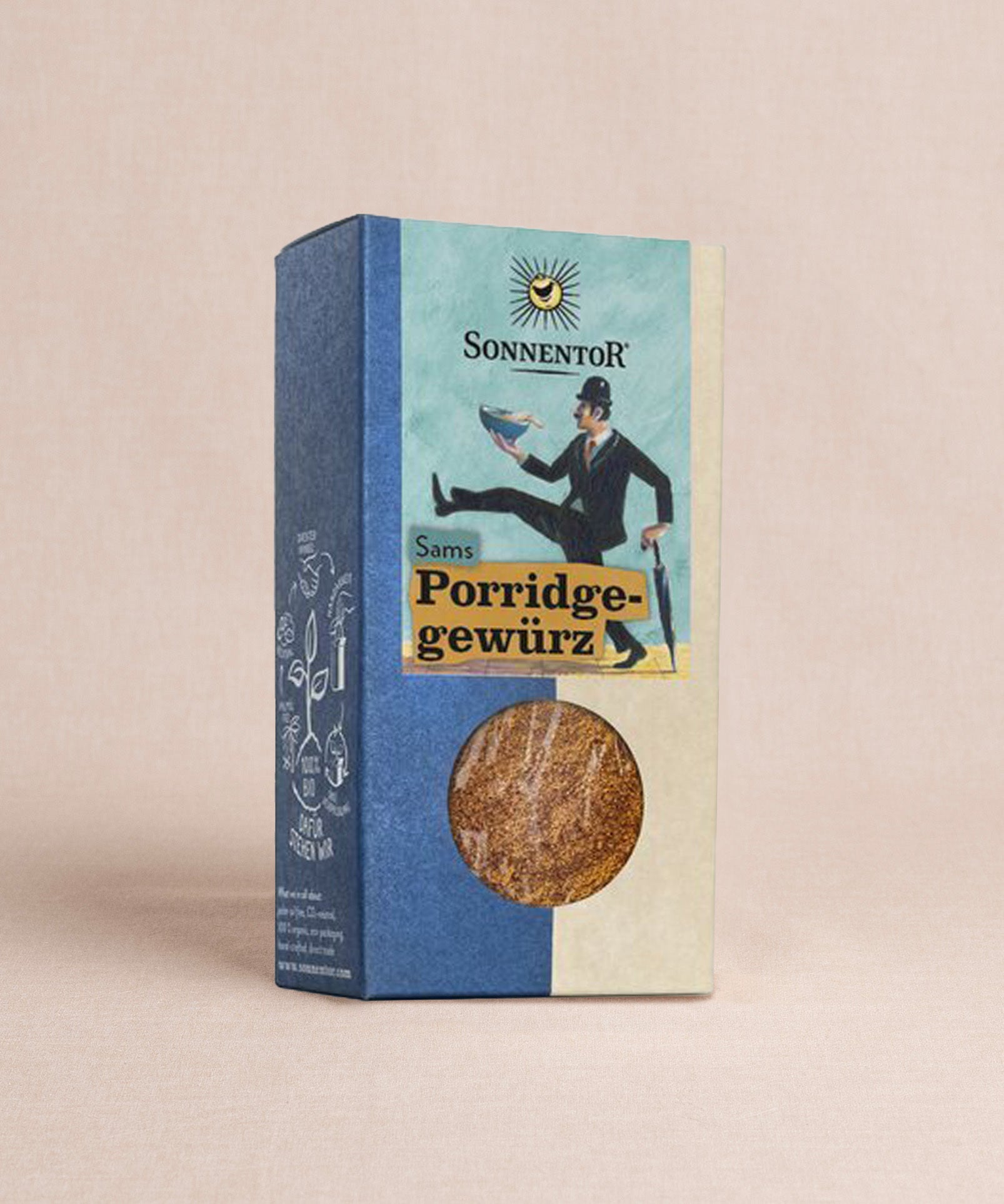 Eine Schachtel Sonnentor Porridge Gewürz ist vor einem schlichten Hintergrund zu sehen. Ein rundes Sichtfeld gibt den Blick auf das Gewürz frei, während verspielte Grafiken die blau-beige Verpackung zieren.