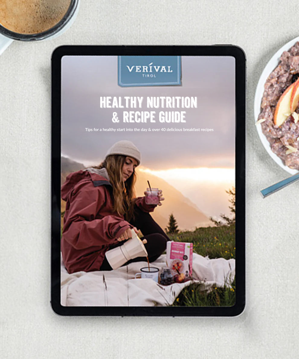 Auf einem Tablet ist der „Kostenloser Ernährungs- und Rezeptguide Deutsch/Englisch (E-Book)“ von Verival Bio zu sehen. Auf dem Titelbild sieht man eine Frau in roter Jacke, die sich bei Sonnenaufgang ein Getränk einschenkt. Neben ihr ist eine Haferflockenschale mit Obst und einem Löffel abgebildet.